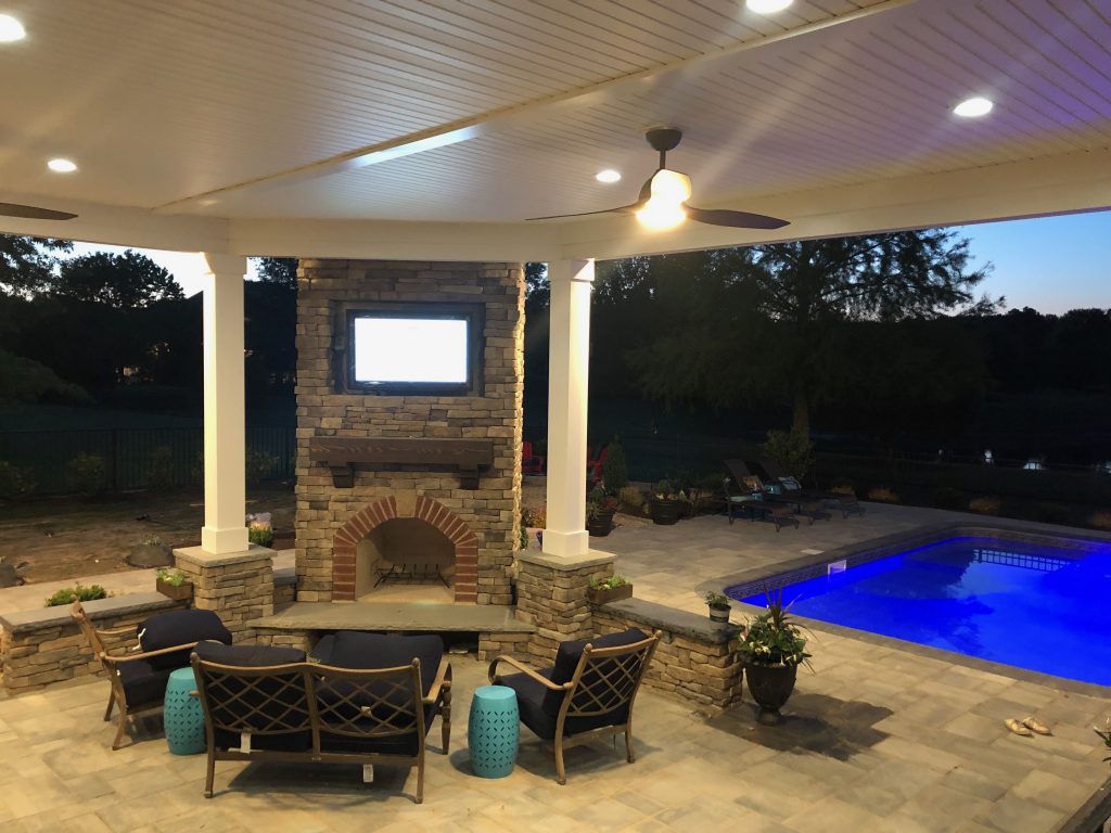 DIY outdoor fireplace built by a homeowner in a corner under a patio cover. This is surrounded by chairs and is poolside.