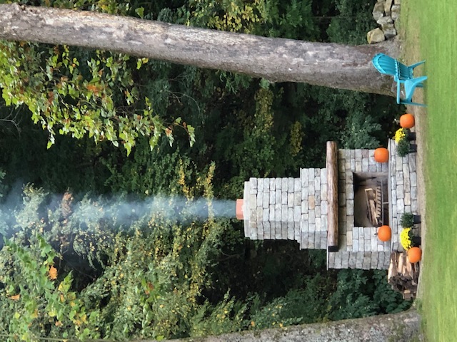 Outdoor DIY fireplace built by a tree line in a backyard.