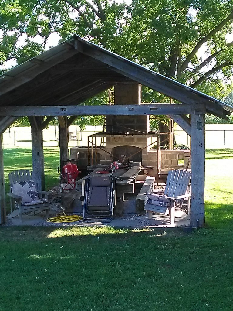 DIY outdoor fireplace built from cinderblocks and mortar under pergola.  Construction zone in backyard of Tombstone design.